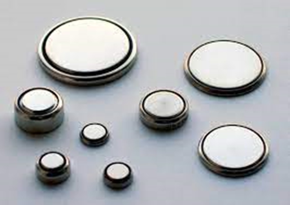 A collection of various coin cell batteries scattered on a wooden surface.