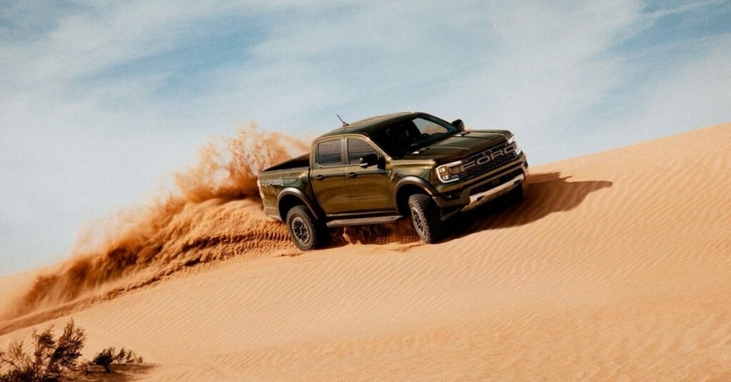 2024 Ford Ranger Raptor scaling a sand dune in a desert environment, showcasing off-road capability.