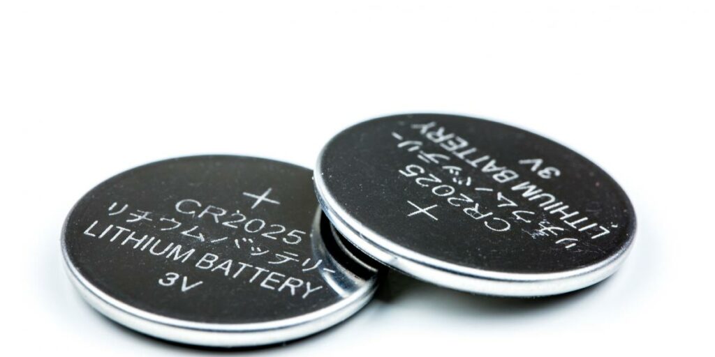 Two CR2025 coin cell batteries placed side by side on a reflective surface.